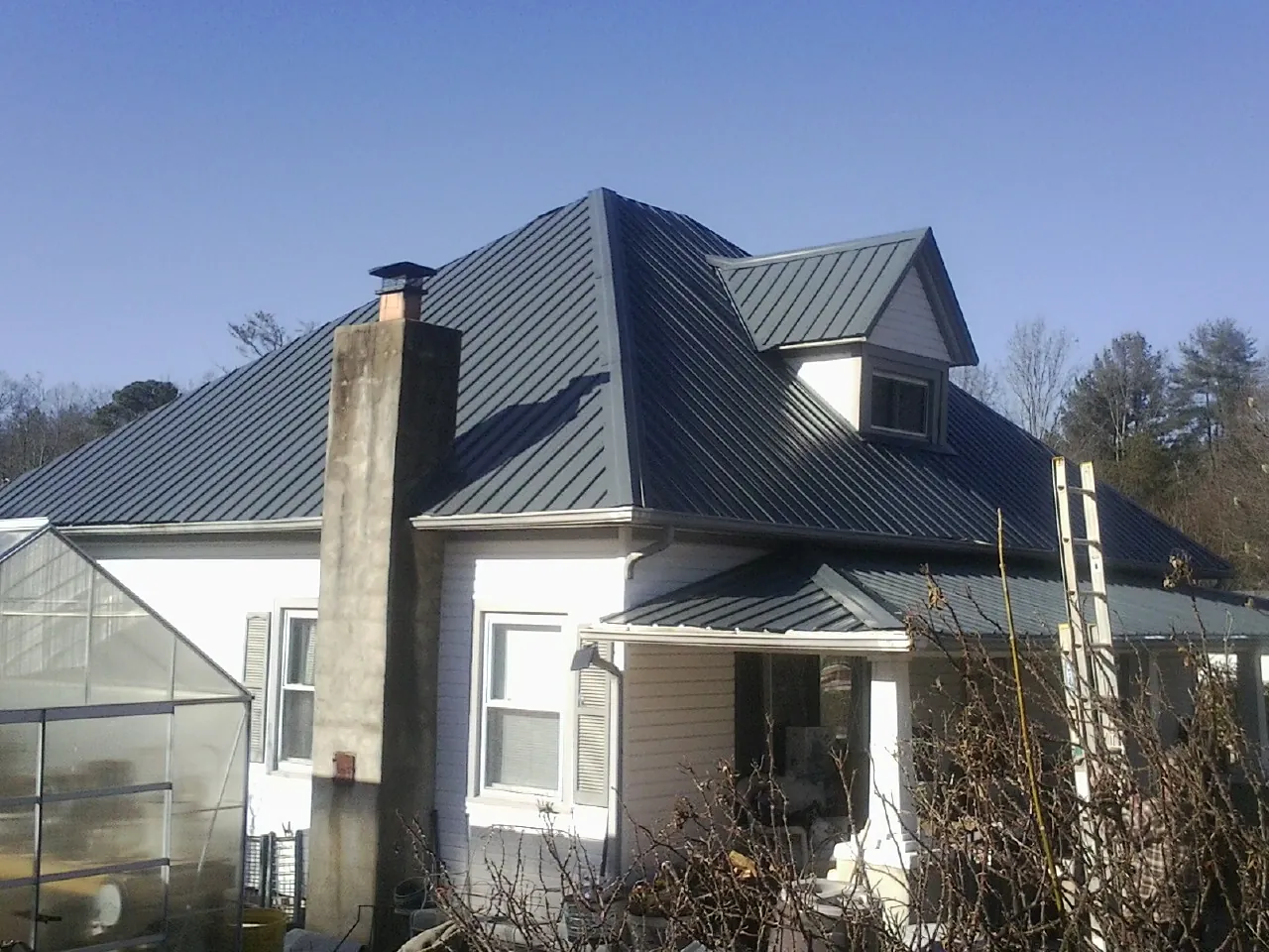 Dark blue standing seam metal roof on a white farmhouse with dormer — Slate & Tile Roof Repair by Roofing Brothers in Elk Mountain