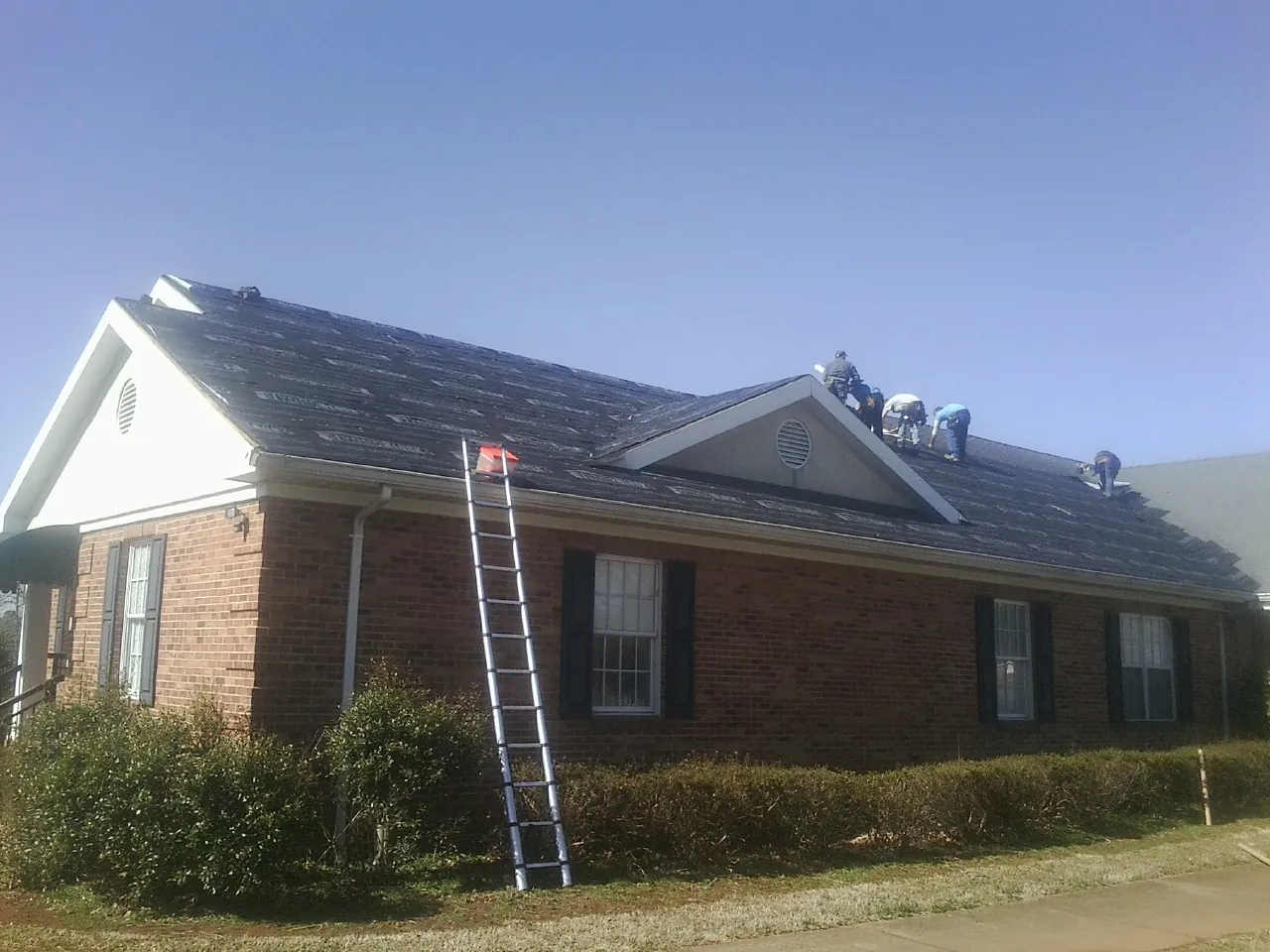 Crew tearing shingles off a brick ranch roof with a ladder set — Emergency Roof Repair work by our crew in Elk Mountain