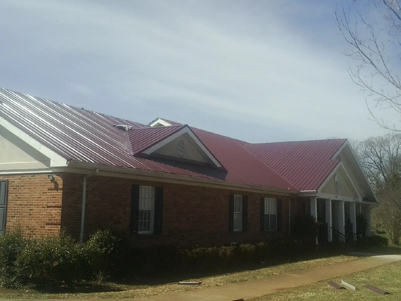 Red metal roof with gabled entries on a long brick building, from a Hail Damage Roof Repair job in Elk Mountain