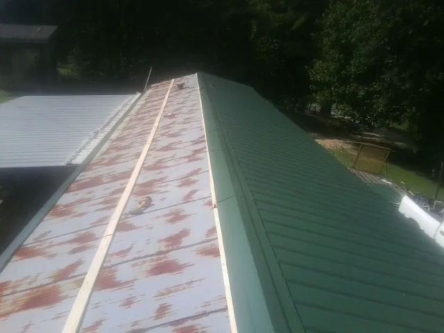 Old rusted panels beside newly installed green metal roofing — Wind Damage Roof Repair by Roofing Brothers in Elk Mountain