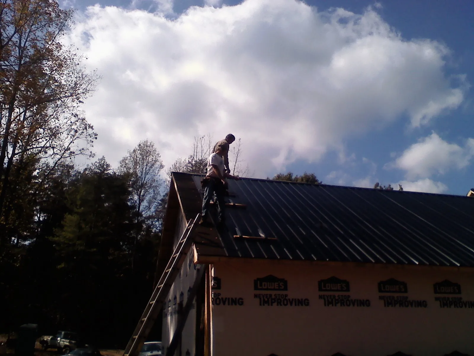 Roofer fastening dark metal panels high against a cloudy sky, from a Roof Inspection job in Elk Mountain